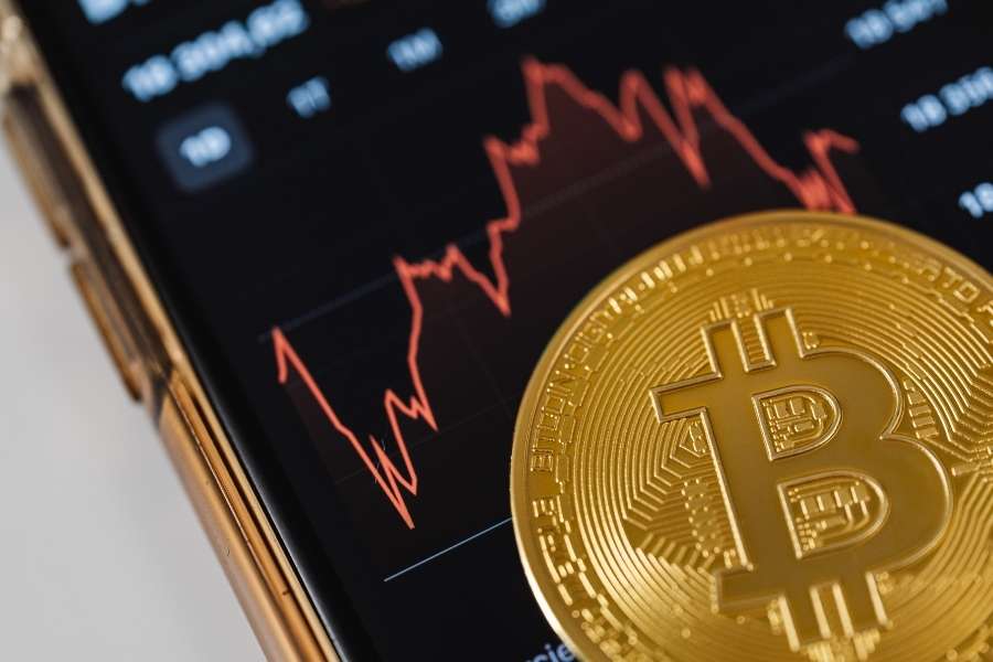 Pièce de Bitcoin dorée posée sur un smartphone affichant un graphique financier pour stocker les actifs numériques.