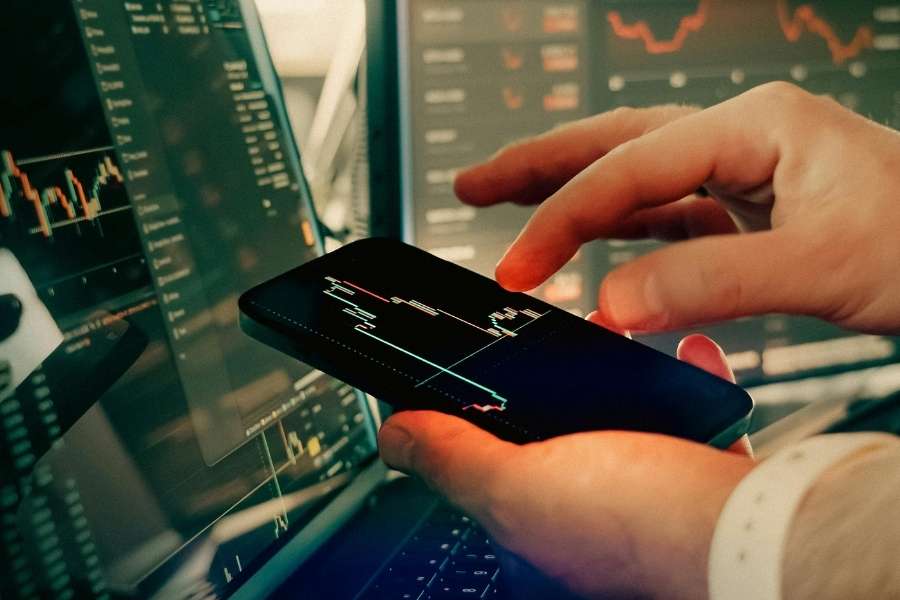 Une personne utilise un smartphone pour analyser les graphiques des monnaies numériques sur un ordinateur.