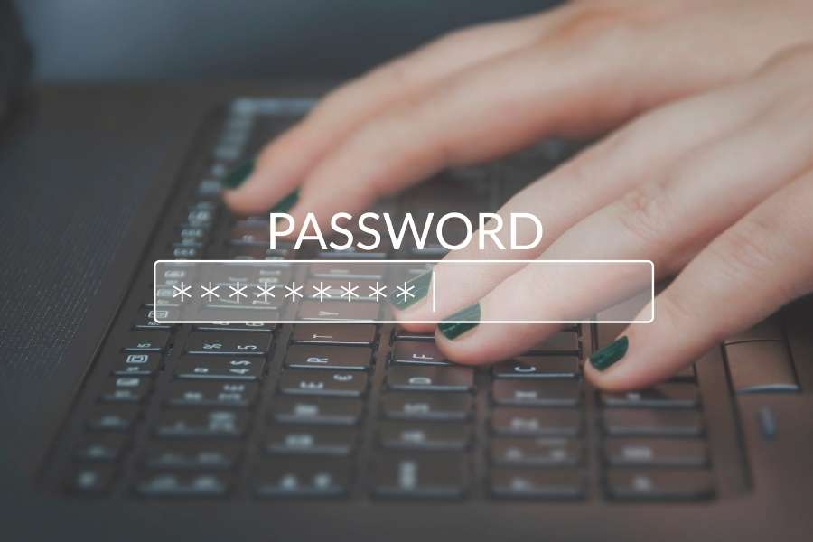 Une main avec des ongles peints en vert tape un mot de passe masqué sur un clavier d'ordinateur portable, illustrant la sécurité de la gestion des mots de passe.